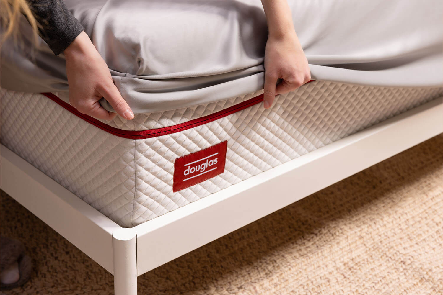 Woman pulling the fitted sheet of her Douglas Bamboo Sheets over the corner on a Juno mattress