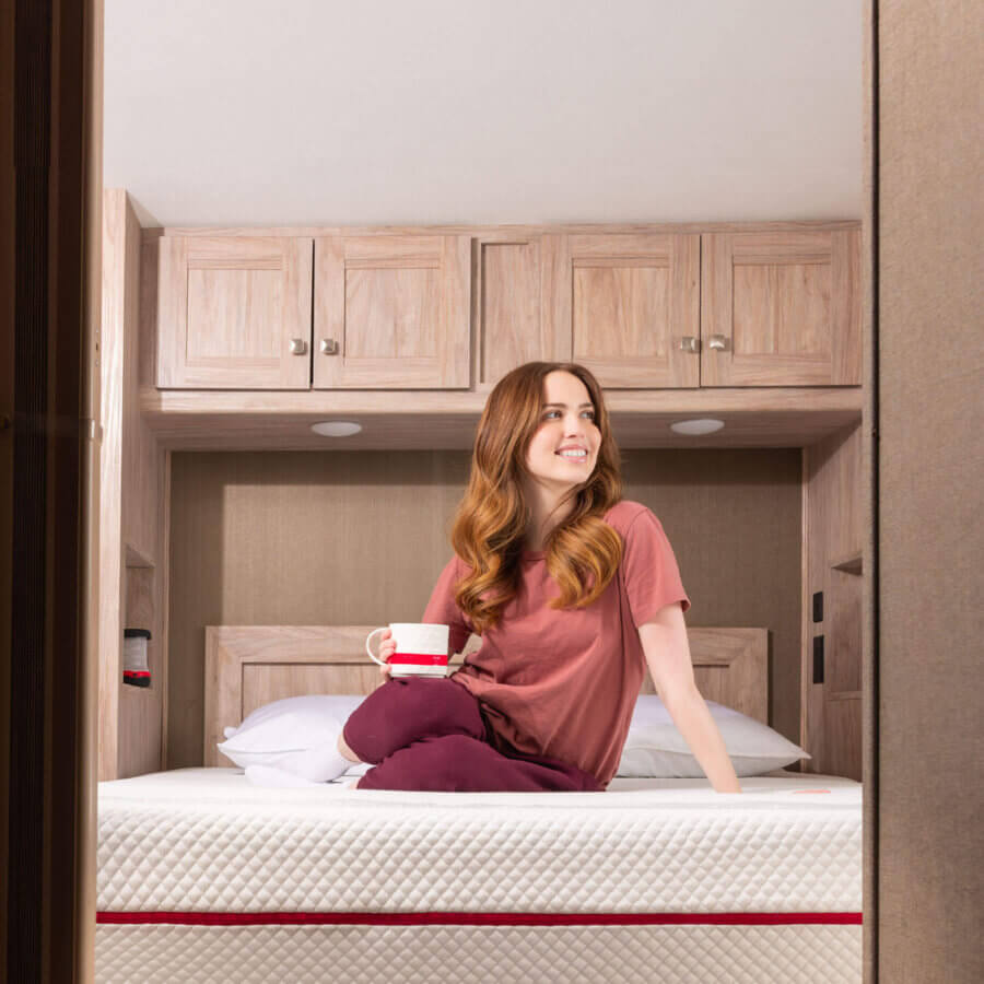 Woman sitting and smiling on a Douglas RV mattress in an RV bedroom