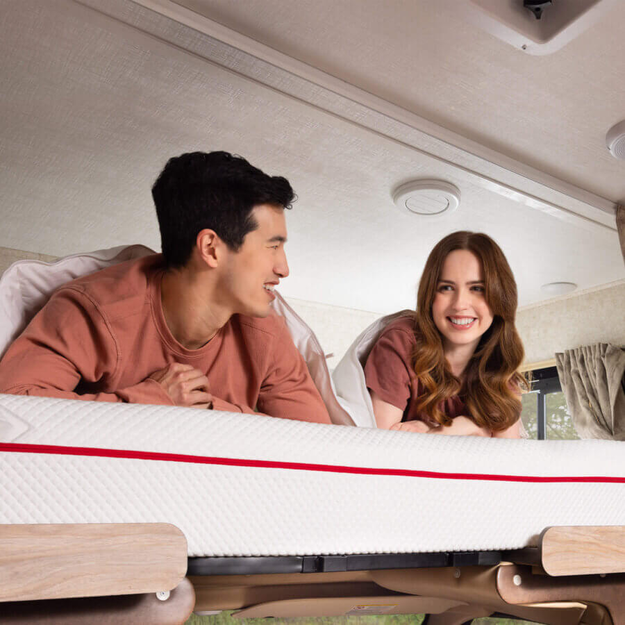 A man and a woman lying on a Douglas RV mattress on the top bunk of a motorhome