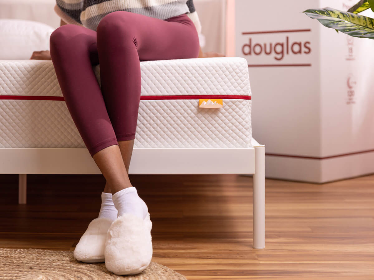 A woman sits on the supportive edge of a Douglas mattress