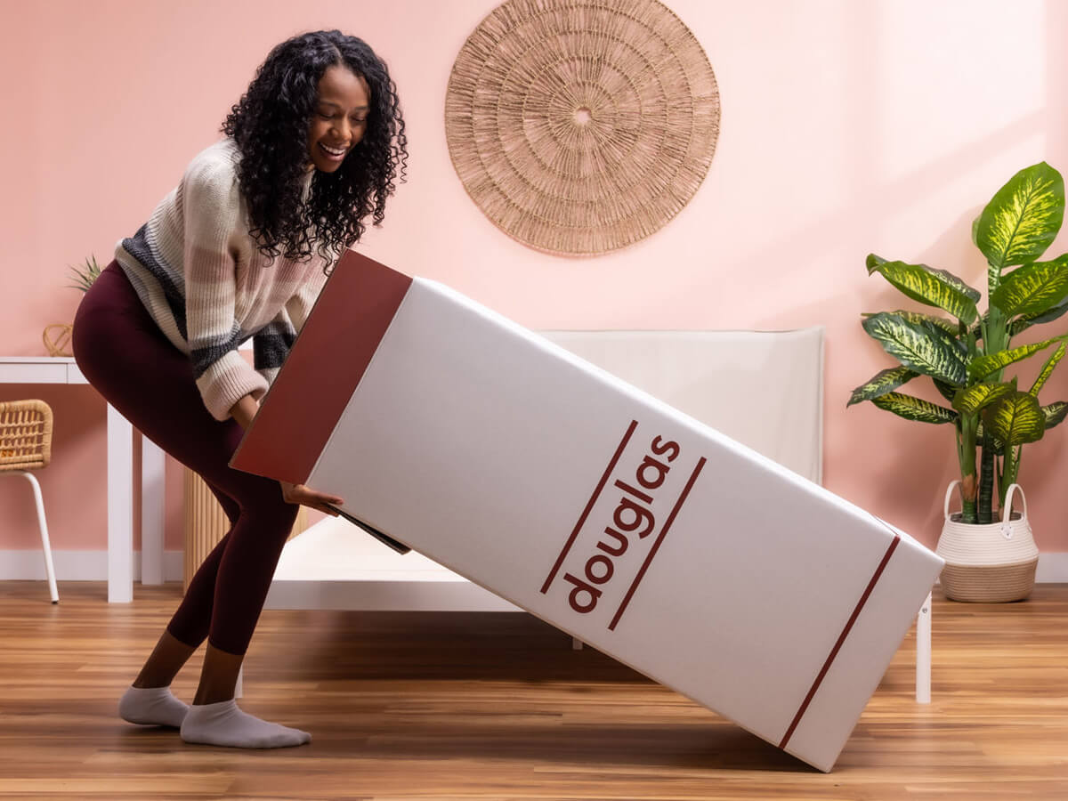 A happy woman unboxes a Douglas mattress in her bedroom