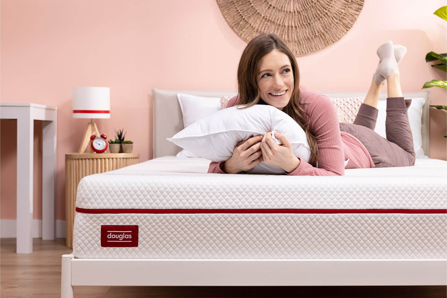 A woman clutches a Douglas pillow and smiles as she lays on her Douglas mattress.