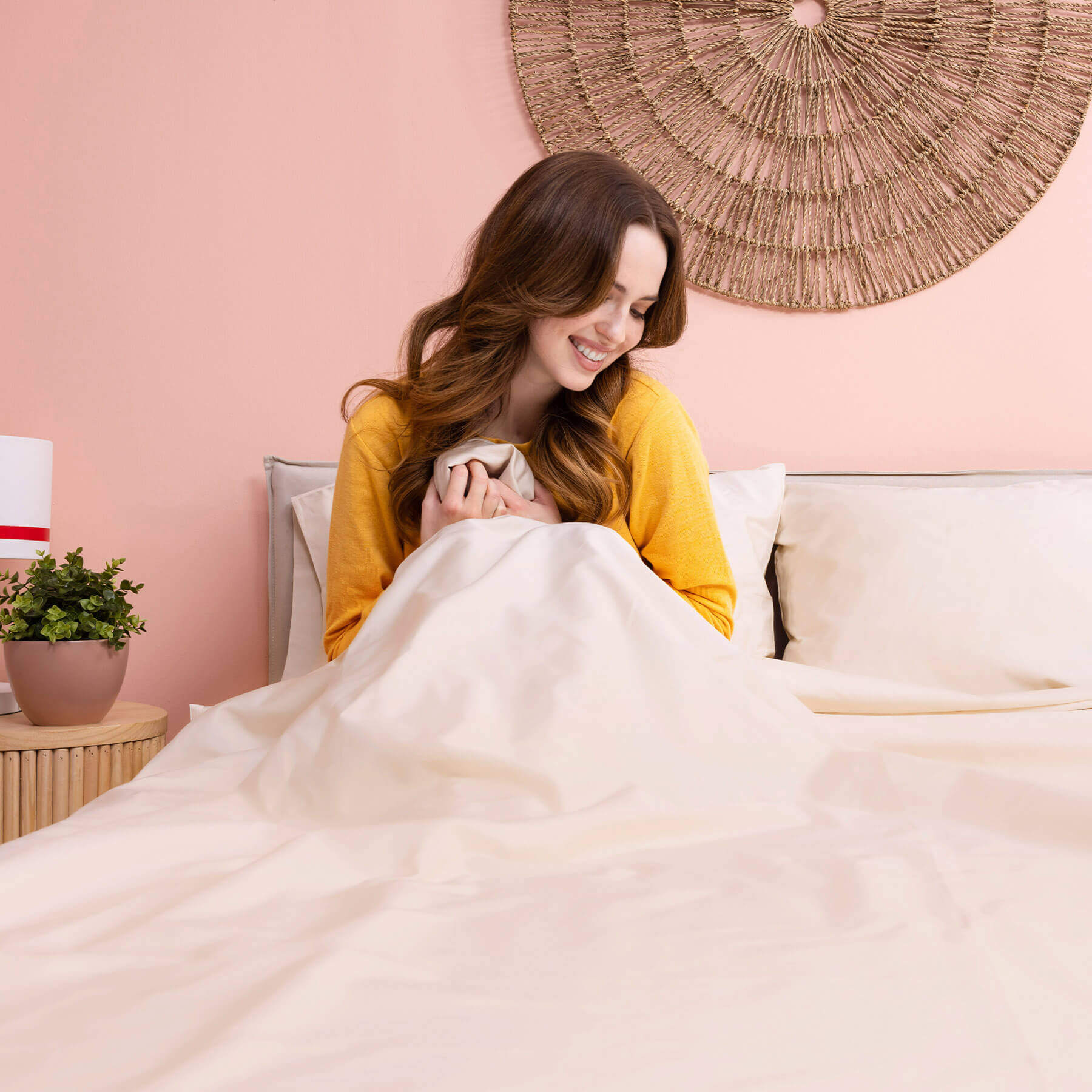 egyptian-cotton-sheets-carousel-5 Woman smiling and sitting in bed, touching her Douglas Egyptian Cotton Sheets