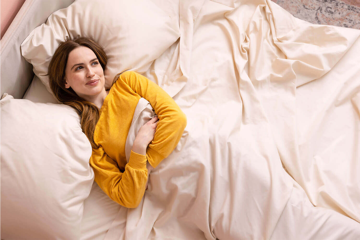 Femme allongée dans son lit et serrant ses draps en coton égyptien Douglas