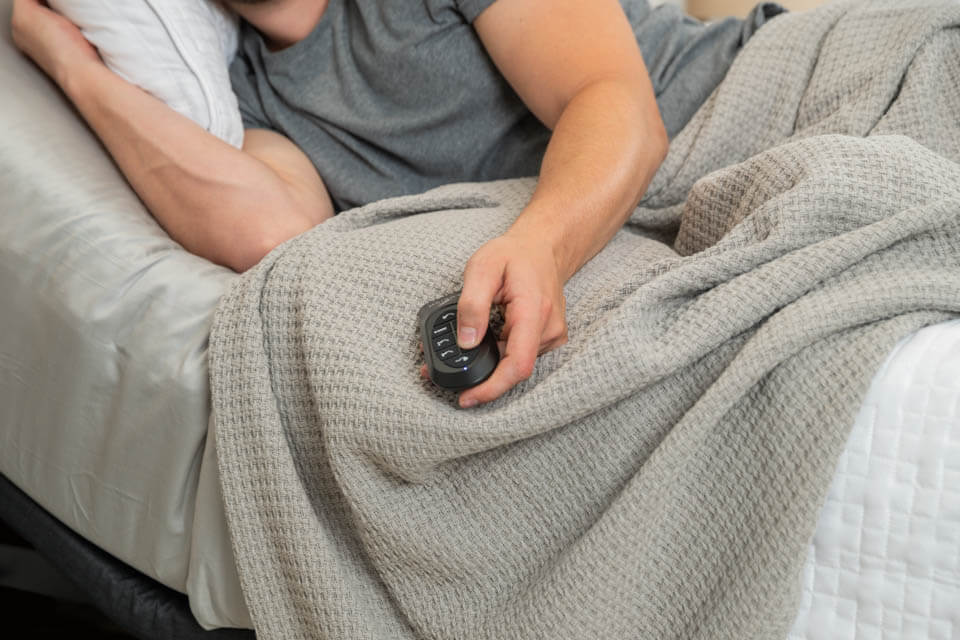 Un homme est couché dans un lit et tient la télécommande de son lit ajustable Podium.